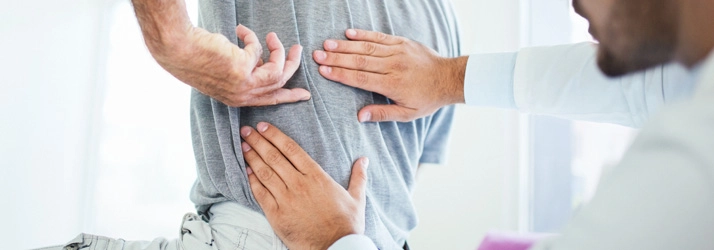 A person pointing to their middle back as a chiropractor looks.